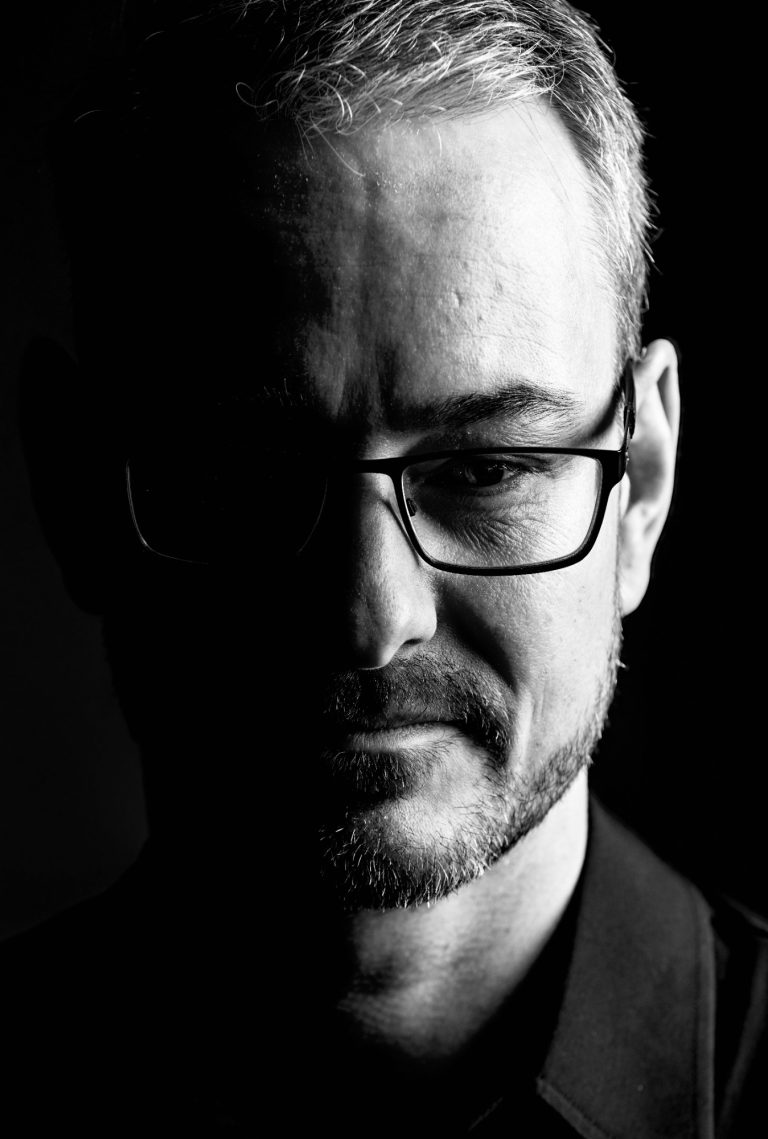 Pressebilder Schwarz-weiß Portrait eines Mannes mit Brille, teilweise im Schatten.
